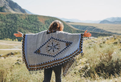 Brunette young woman traveler in poncho from back on road, trip to mountains, altai