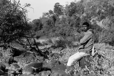 Side view of young man sitting on rock