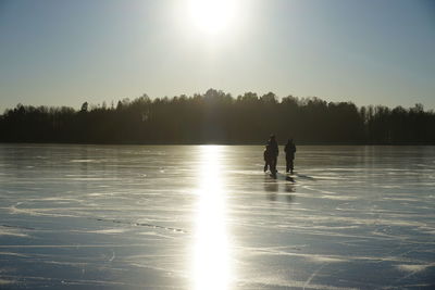 People ice-skating on frozen lake against sky during sunny day