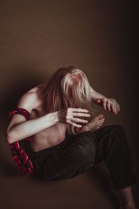 Shirtless man sitting against brown background