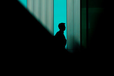 Side view of silhouette man standing against lined shadow blue green wall 