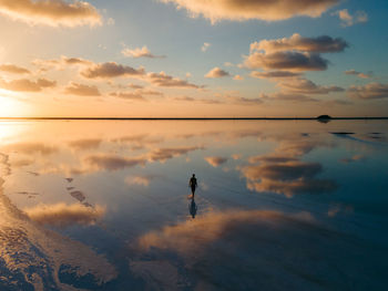 Aerial photo of a person walking across salt flats reflecting dramatic sunset and clouds in mexico.