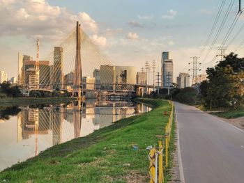 Road by river and buildings against sky