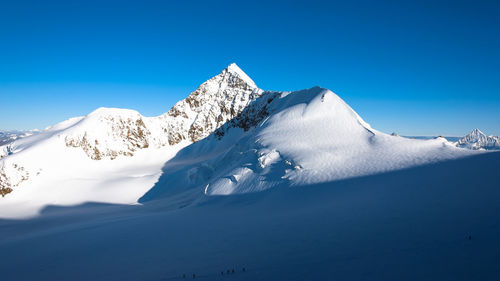 Low angle view of snowcapped mountains against clear blue sky