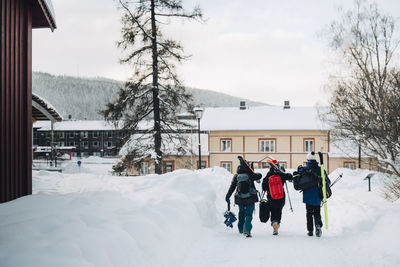 Full length rear view of friends wearing backpack while walking on snow at ski resort