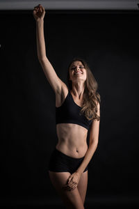 Smiling young woman with hand in hair standing against black background