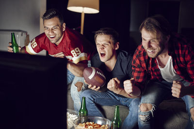 Friends cheering while looking at television set in living room