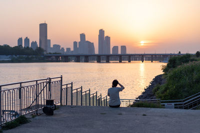 Rear view of woman standing on pier over river against sky at sunset