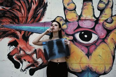 Young woman smoking cigarette and covering breast with medical x-ray while standing against graffiti wall