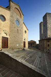 Low angle view of historic building against blue sky, san geminiano, tuscany, italy