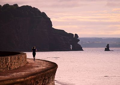 Silhouette man standing on cliff by sea against sky