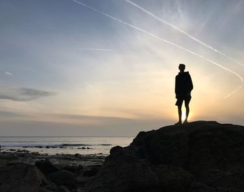 Silhouette man standing on rock at beach against sky during sunset