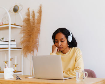 Sleepy african-american female student in headphones attending online lecture on laptop at home