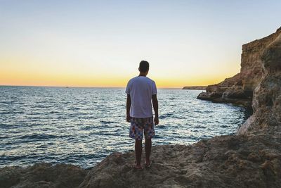 Rear view of man looking at sea against clear sky