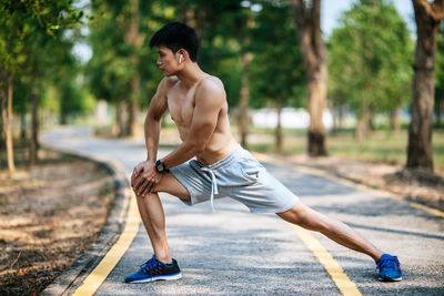 Side view of shirtless young man skateboarding on road