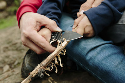 Midsection of father assisting son in cutting wood at newbury park