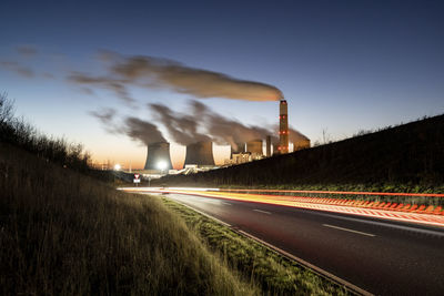 Uk, england, nottingham, light trails stretching along asphalt road at dusk with coal-fired power station in background