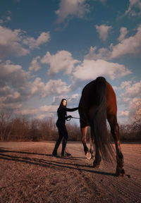 Full length portrait of woman standing by horse against sky