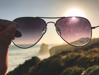 Close-up of hand holding sunglasses against sky