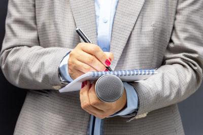Midsection of woman writing in diary while holding mic
