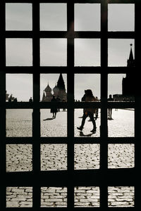 Silhouette people by buildings against sky seen through window