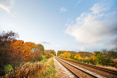 Railroad track amidst trees against sky during autumn