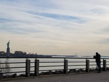 Rear view of man standing by railing in sea against sky