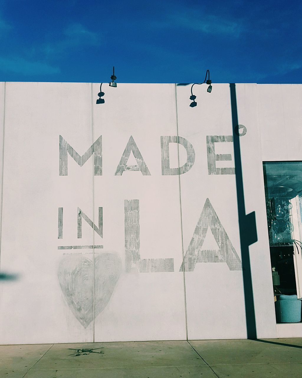 built structure, architecture, building exterior, blue, sunlight, guidance, day, text, western script, communication, shadow, wall - building feature, white color, outdoors, no people, sky, cross, sign, street, wall