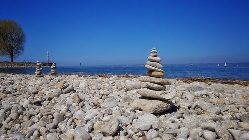 Stack of pebbles on beach against clear blue sky