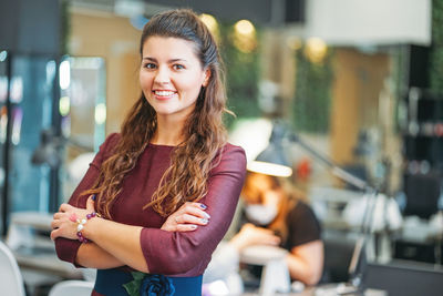 Portrait of smiling young woman standing with arms crossed