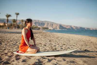 Woman sitting on surfboard at beach