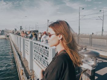 Side view of woman against railing against sky