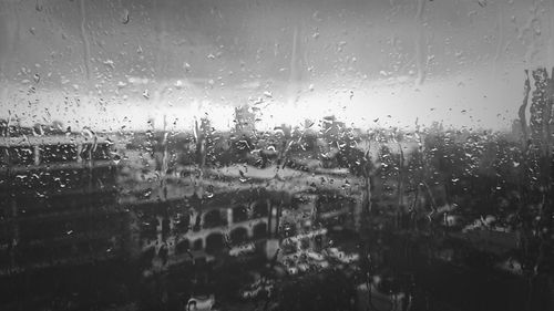 Close-up of wet glass window against sky