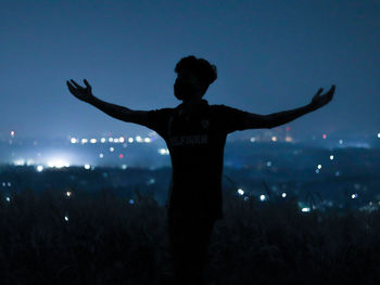 Rear view of silhouette man standing against sky at night