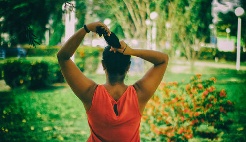 Rear view of young woman tying hair while standing against trees in park