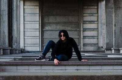 Portrait of woman wearing sunglasses while sitting below bridge