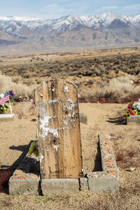 Weathered wood grave marker in desert and mountains against sky