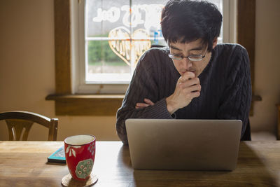 A man sits at a dining room table on computer working from home