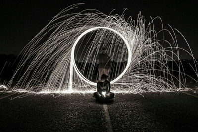 Man making light painting while woman sitting on road at night