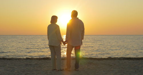 Friends standing on beach against sky during sunset