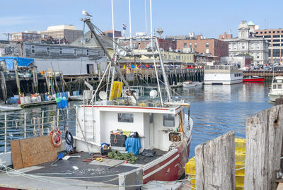 Sailboats moored in harbor by buildings in city against sky