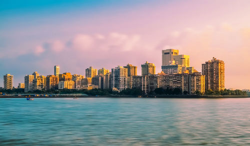 Sea by buildings against sky during sunset