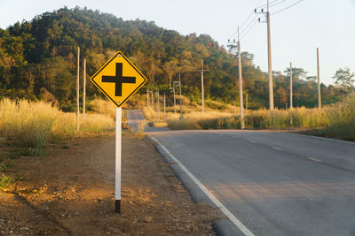 Road sign by trees against sky