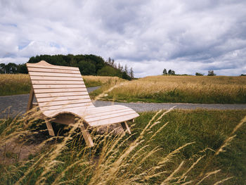 Bench in field against sky