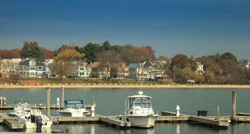 Sailboats moored on sea by buildings against sky