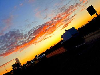 Silhouette road against orange sky