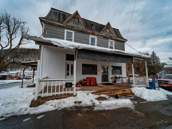 Snow covered house by building against sky