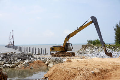 Earth mover at beach against sky