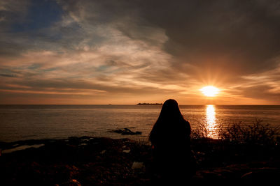 Silhouette person looking at sea against sky during sunset