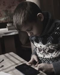 A boy in a christmas sweater sits at a table and plays games on a mobile phone